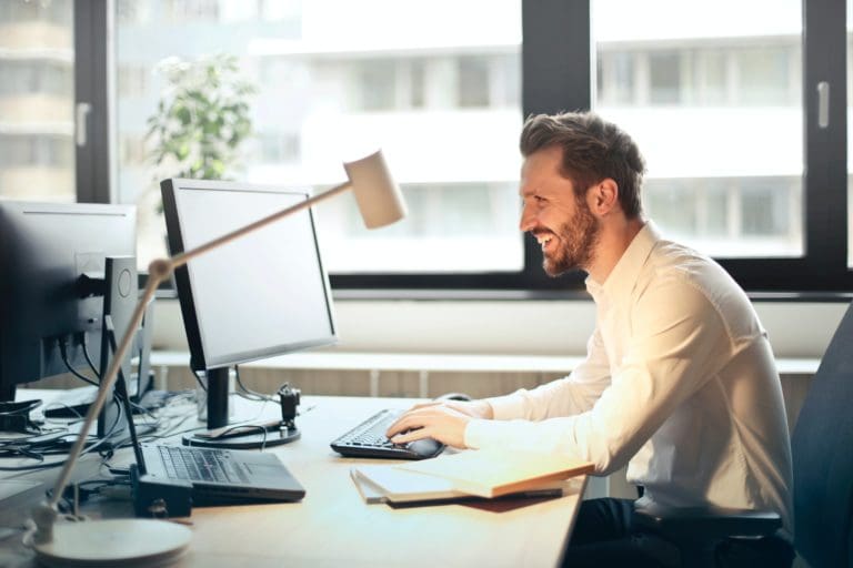 Man in white suite working in front of a computer while smiling