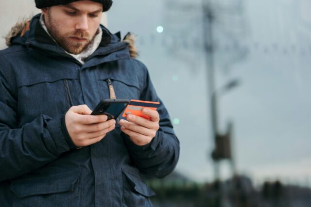 Man typing something on his phone while holding a credit card